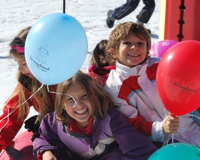 Fröhliche Kinder, die auf einem roten Snowtube mit bunten Luftballons im Schnee Spaß haben.