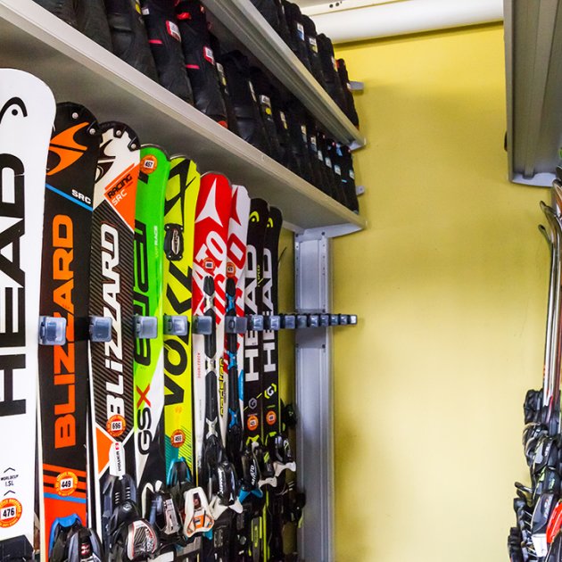 Skier stehen ordentlich aufgereiht in einem Skiraum an Wandhaltern.