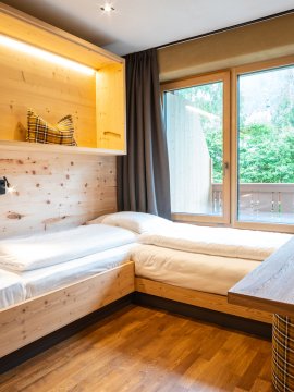 Zimmer mit zwei Einzelbetten, Holzwänden, Balkon und kleinem Tisch